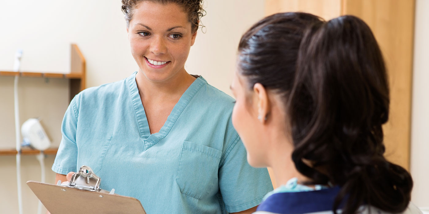 A medical assistant holds a clipboard while asking a patient a question