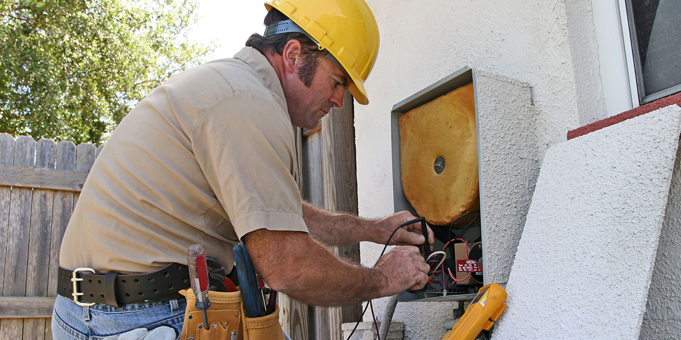 A stock image of a worker wearing a tool belt and a hard hat while working on an HVAC system