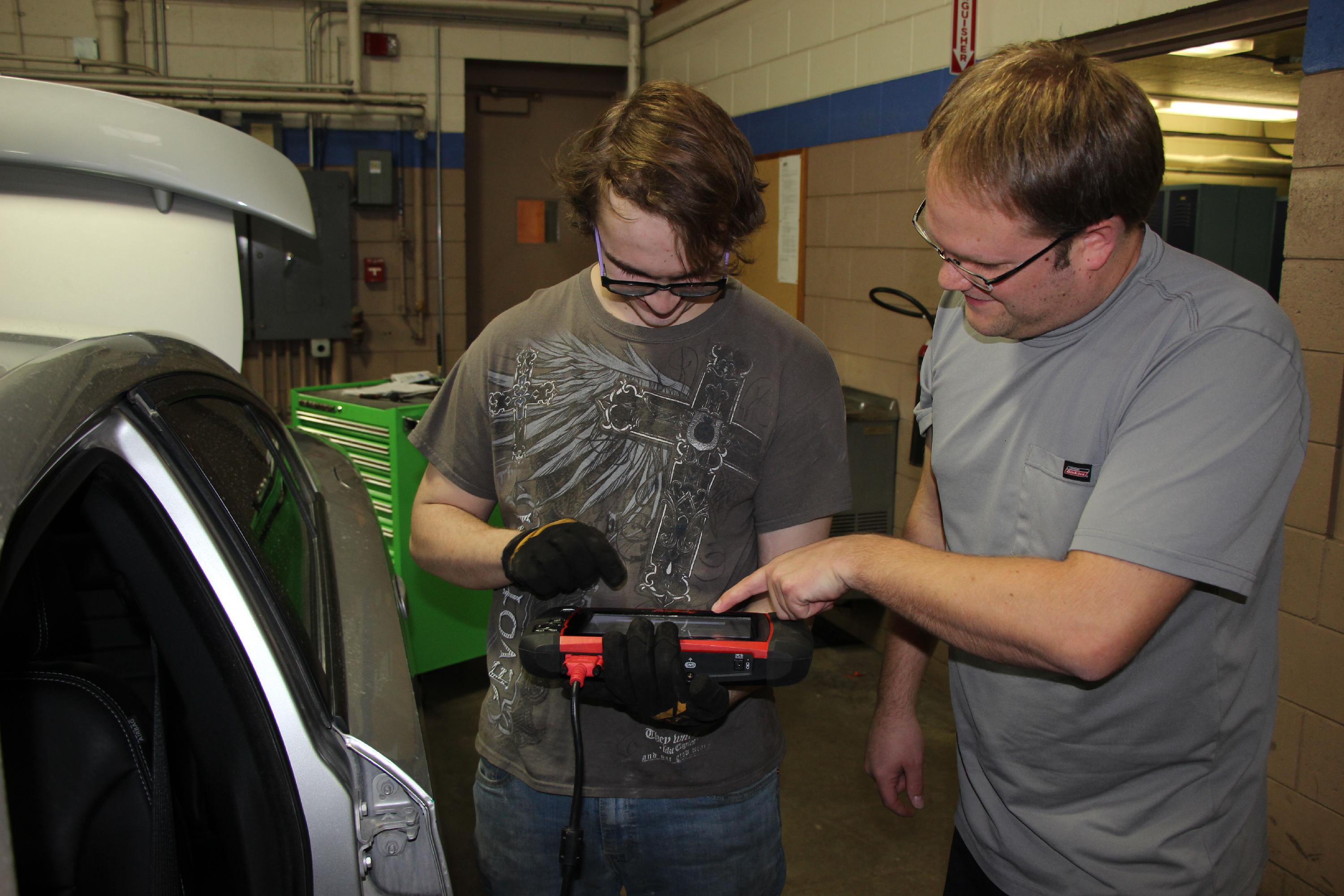 Auto service instructor shows a student how to use a computer system to diagnose an error in a car