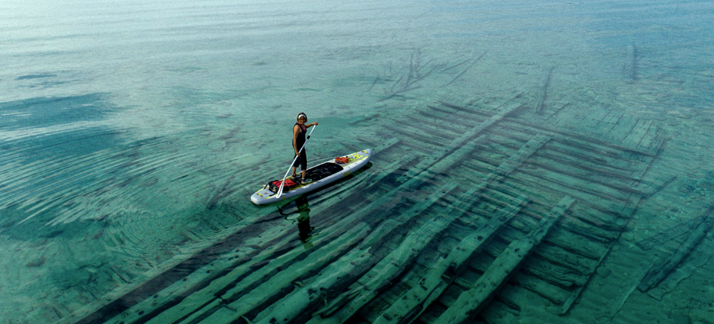 A paddleboarder floats on the water overlooking an abandoned shipwreck