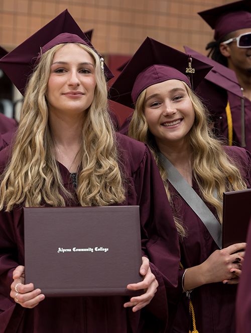 Two female students smile after receiving their diplomas at graduation