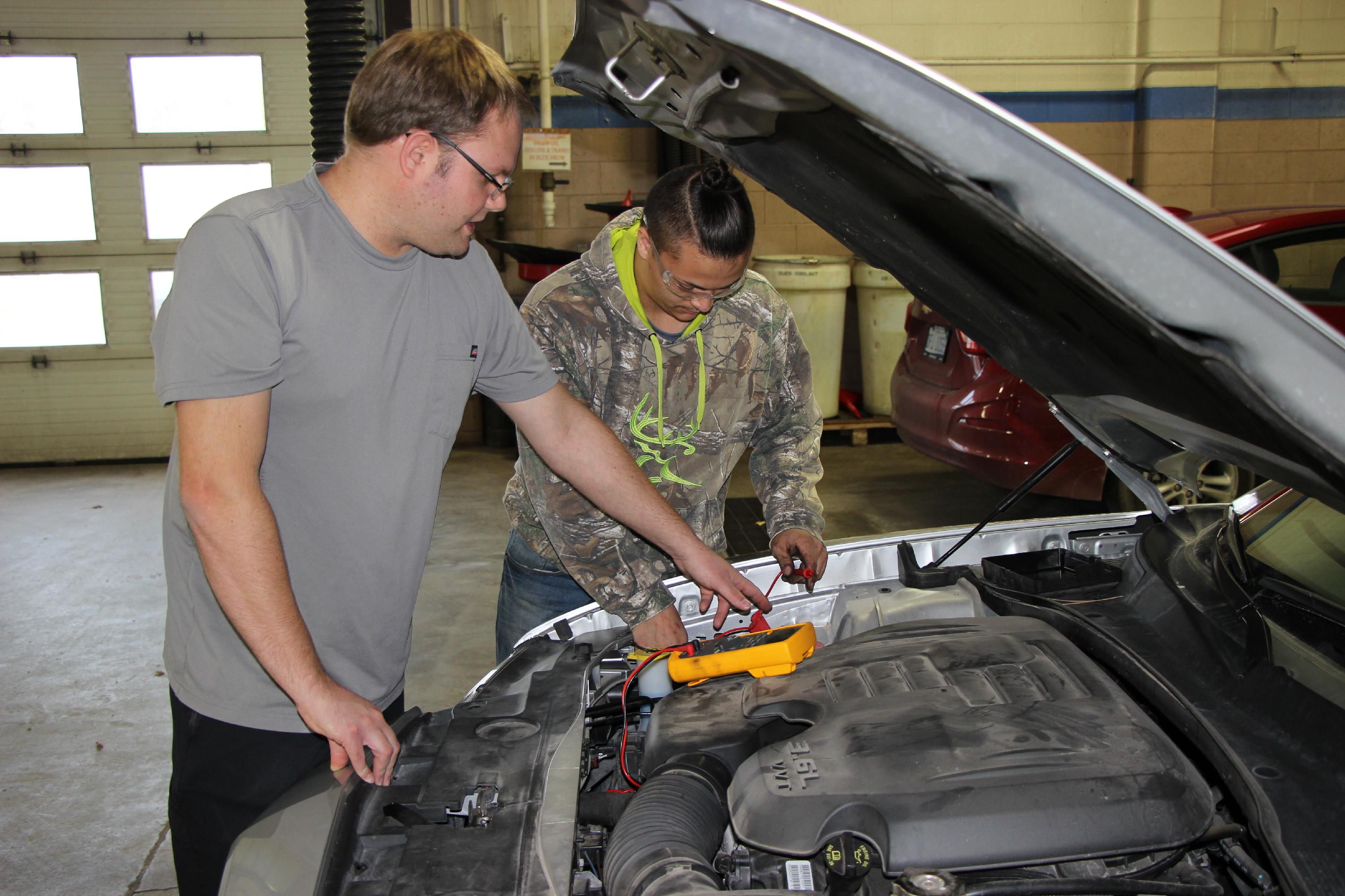 Auto Service instructor works under the hood of a car with a student