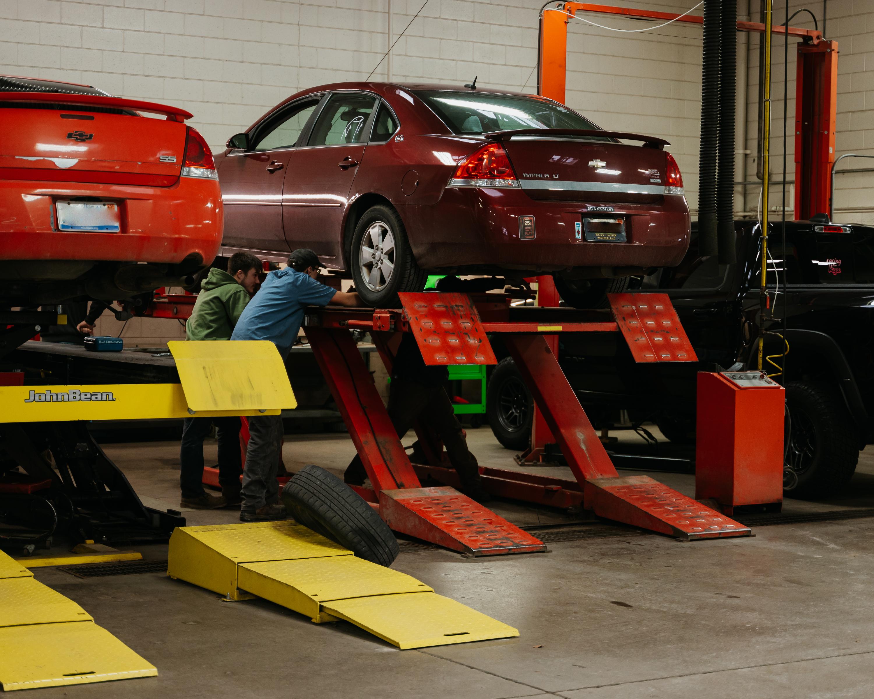 Two vehicles on lift with student working on tire