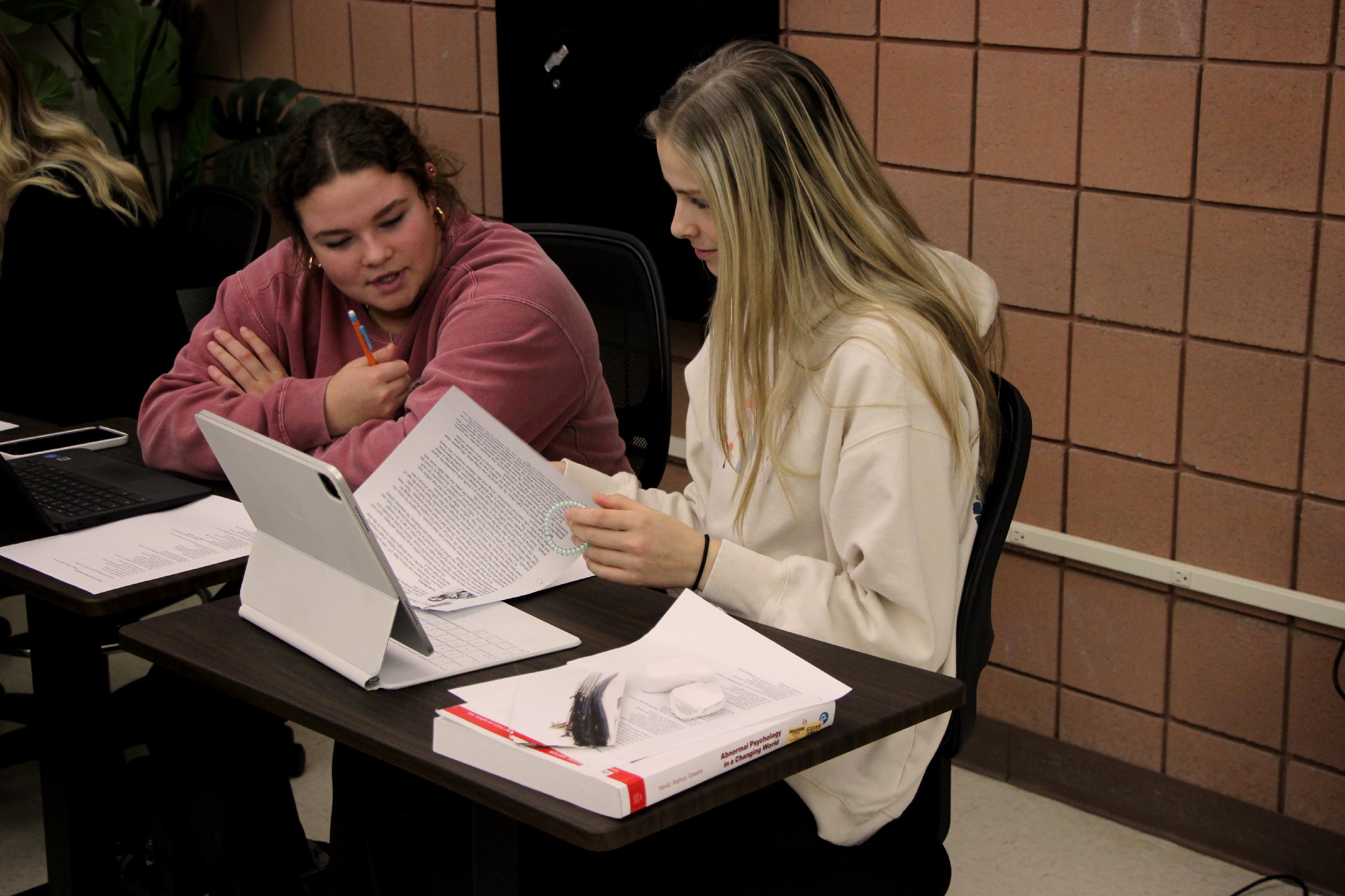 Two students work on an assignment together while looking at a piece of paper
