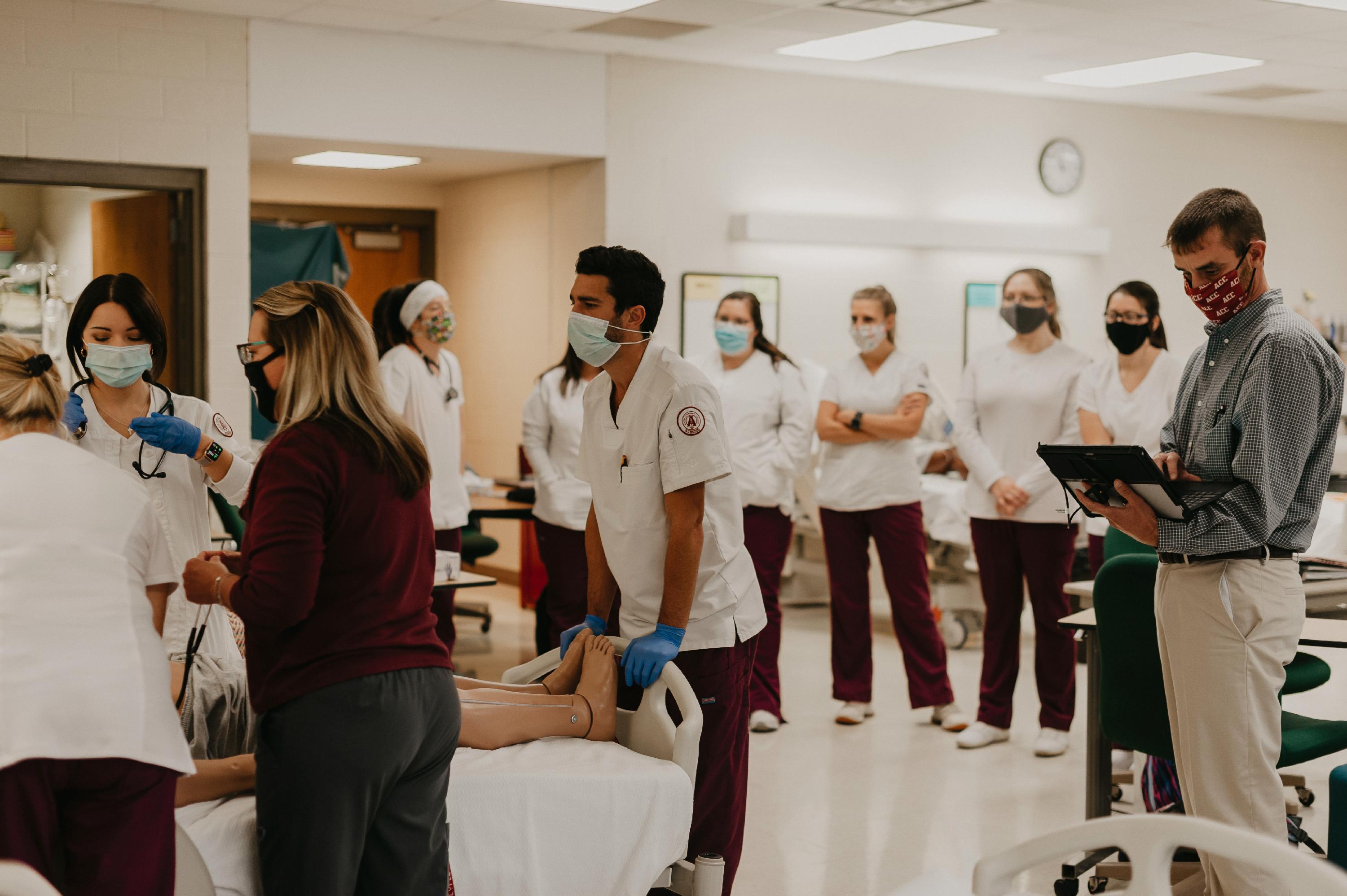 A group of students watch an instructor work with a few students on a manikin