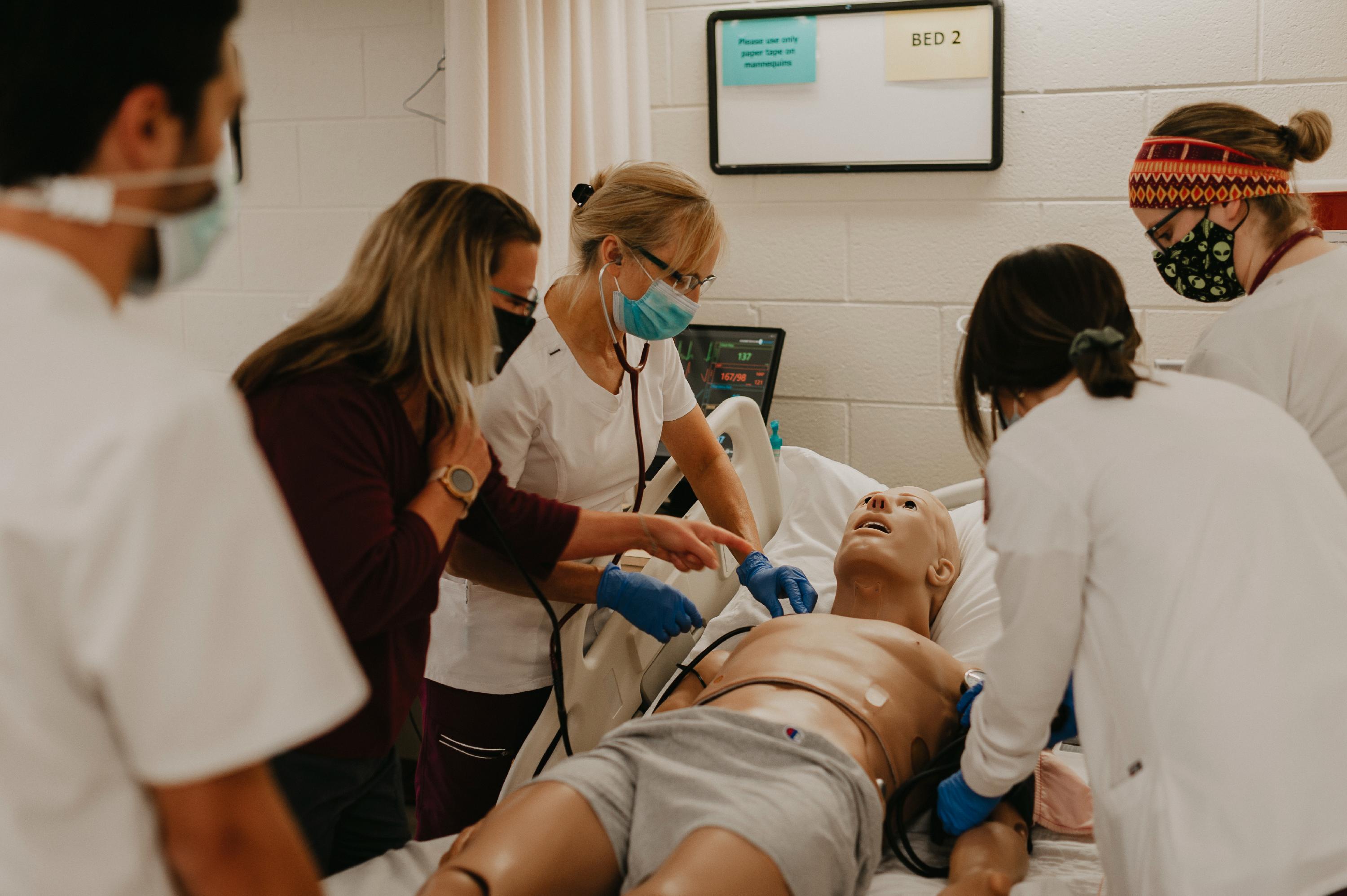 Two instructors demonstrate how to use a stethoscope on a mankin