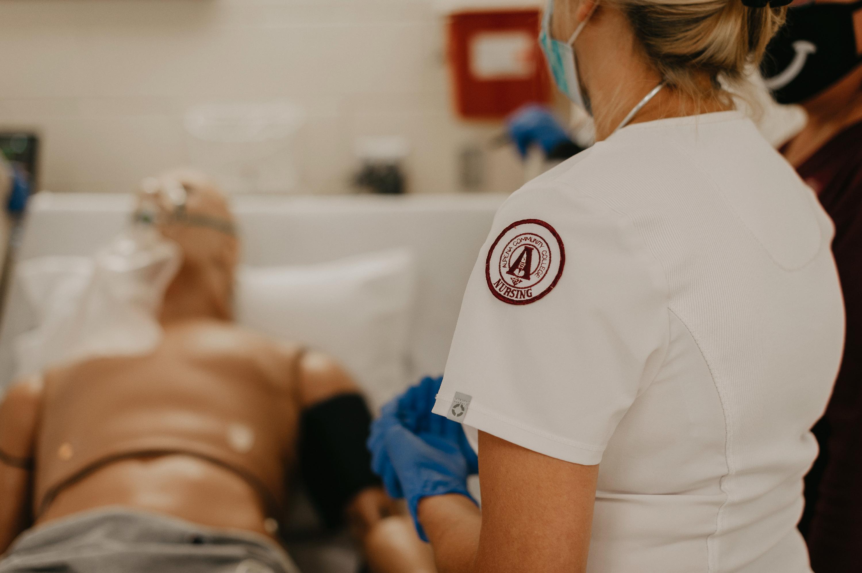 A nursing student stands on the side of a manikin